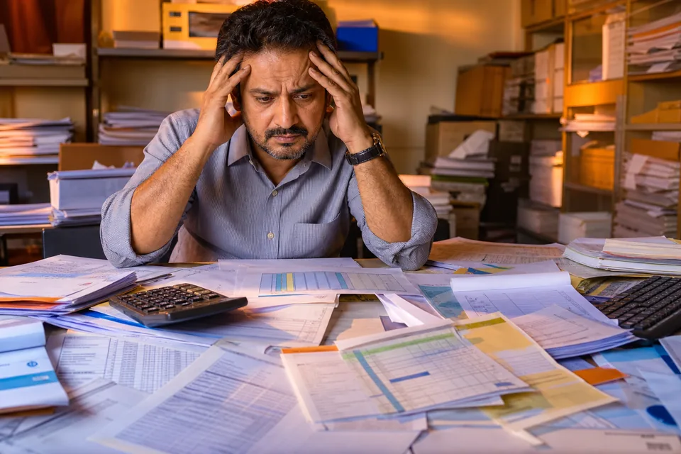 Stressed Indian business owner surrounded by GST invoices, Excel sheets and inventory paperwork